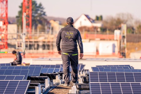 Man on a building with solar panels, industrial environment and a few houses visible, PV