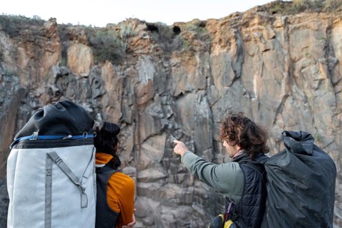 Two climbers equipped with gear discuss their route against a rugged cliff face, embodying the