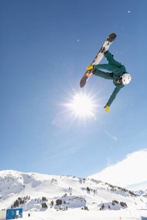 A snowboarder executes an impressive aerial trick in the bright sunshine, showcasing skills above a