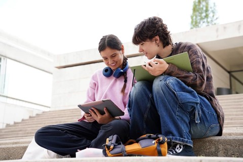 From below two teenagers, a non-binary individual and a female, are engaged in studying while