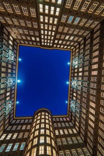 Triangular office building at night, illuminated, with street in the foreground and deep blue sky,