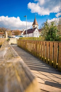 The wooden walkway and fence lead to the village church on a sunny day with clear skies,