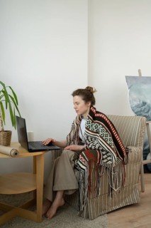 A woman sits comfortably in a striped armchair, wrapped in a patterned blanket. She focuses on her