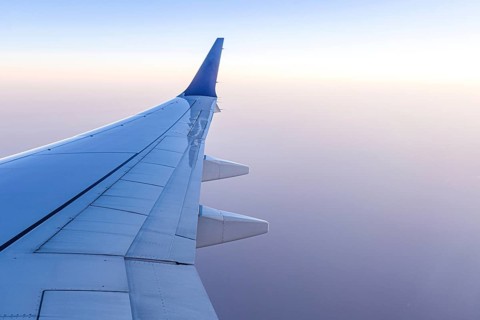 A serene view from an airplane window showing the aircraft wing gliding high above the clouds. The