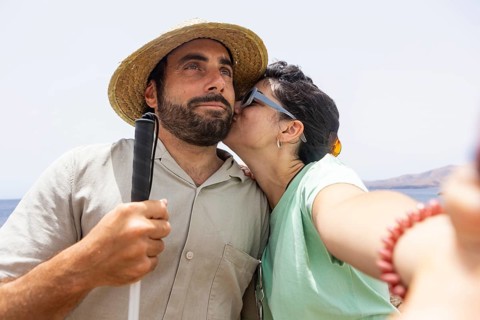 A touching moment as a woman kisses a blind man on the cheek while they take a selfie together by