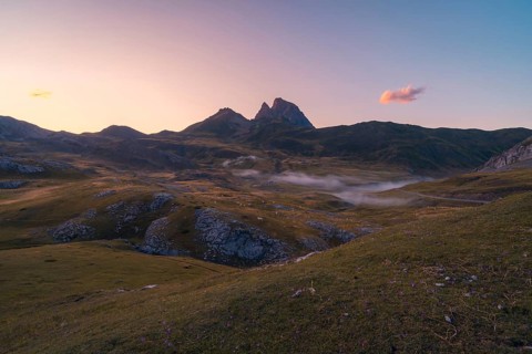 A serene mountain landscape at sunset with mist hovering over rolling hills in the Pyrenees. The