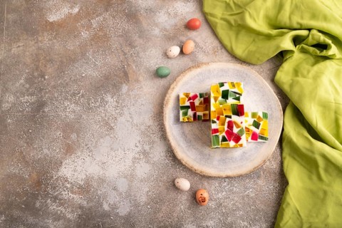 Colored Fruit and milk jelly on brown concrete background and green linen textile, top view, flat