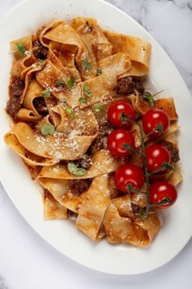 Pappardelle pasta with bolognese sauce, topped with parmesan cheese and cherry branch, homemade, no