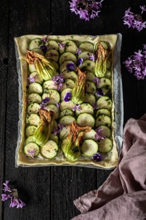A beautifully arranged zucchini and edible flower tart on a rustic wooden table. The vibrant colors