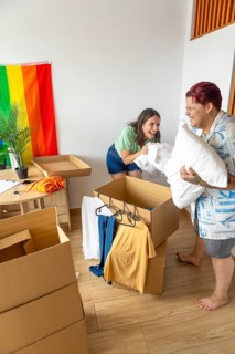 Lesbian friends are joyfully unpacking clothes and pillows into boxes in a bright apartment in a