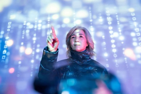 An elderly Asian woman engages with the immersive metaverse, her finger pointing at glowing digital