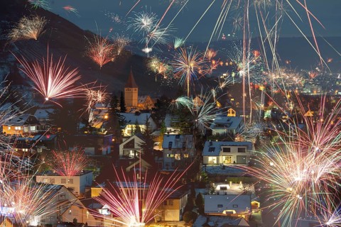 Night scene with fireworks over a village, colorful rockets in the sky, houses illuminated with