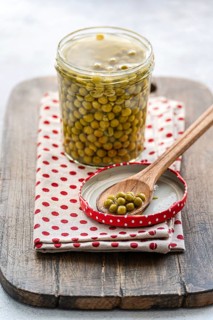 A glass jar of green homemade organic peas displayed on a rustic wooden board, topped with a wooden