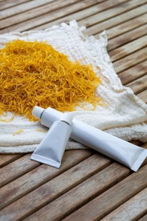 Two white tubes of marigold petals cream placed on a wooden surface next to a pile of dried yellow