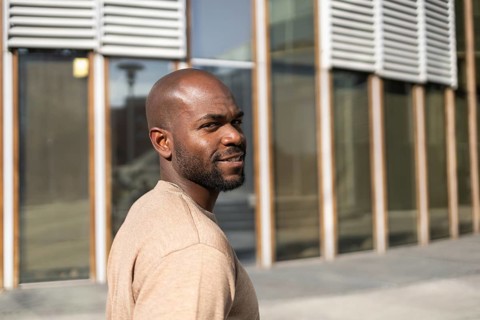 A cuban man is seen smiling, walking outdoors in a city setting with modern architecture in the