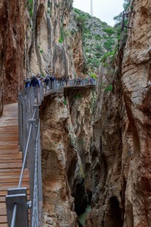 Wooden bridge of the Caminito del Rey along an impressive gorge with hikers and steep rock faces,