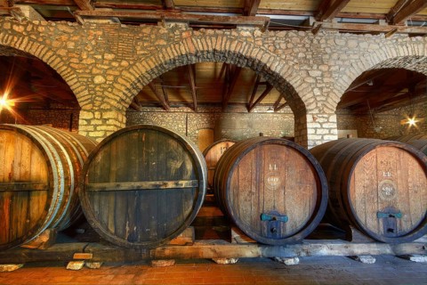 Large wooden barrels in a rustic wine cellar with brick vaults and warm light, Achaia Clauss