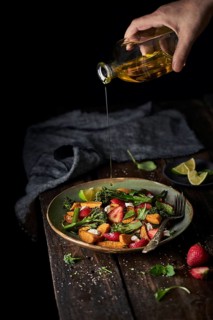 From above crop faceless person pouring olive oil from bottle on summer tasty fresh mixed salad