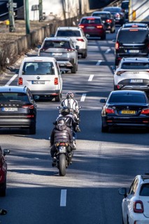 Motorcyclists overtake the partly stationary, partly slow-moving traffic in the middle of the