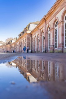 Historic building reflected in a puddle of water under a bright blue sky, Schwetzingen Palace
