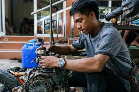 Young mechanic focused on motorcycle engine repair outdoors. Wearing casual attire, he concentrates