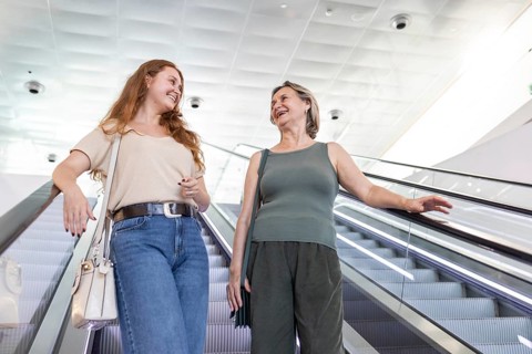 A joyful mom and daughter pair share a moment on an escalator, embodying a relaxed and delightful
