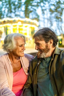 Vertical photo of a modern caucasian senior couple looking at each other sitting on night city fair