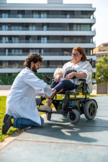 Doctor adjusting footrest of electric wheelchair for smiling disabled woman in park, promoting