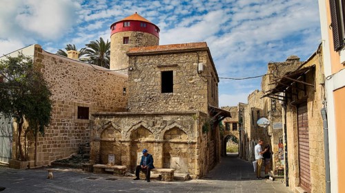 Older buildings in an old town with a red tower and people on benches, Rhodes Old Town, Rhodes,