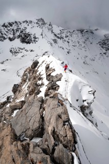 Mountaineer descending the narrow ridge of Piz Laviner, view of mountain panorama in wintry