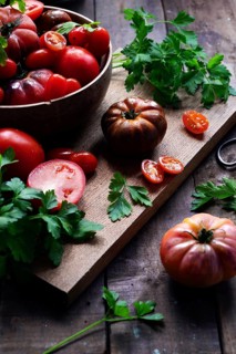 A rustic display of fresh tomatoes and vibrant parsley arranged on a wooden cutting board. The deep