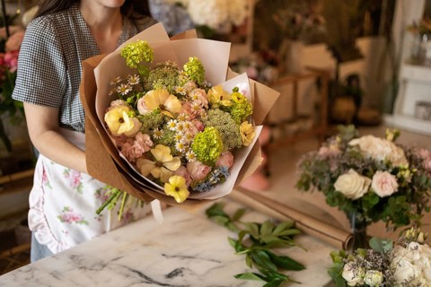 A woman holds a vibrant bouquet of flowers in a flower shop. The scene captures the lush variety of