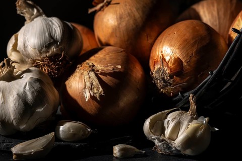 Onions and garlic in a basket, arranged in warm light on a dark background