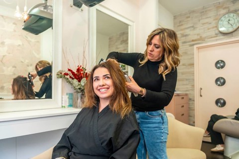 Hair stylist curling a smiling young woman's brown hair with a heated tool in a modern salon,