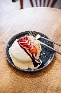 Fluffy japanese pancakes topped with sliced strawberries, creamy sauce, and syrup on a round plate.