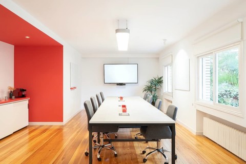 Bright conference room in office with a long table, chairs, and a vibrant red accent wall. Features