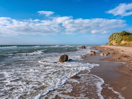 Unspoiled secluded stretch of coast with cliffs and boulders in the surf on the beach of the stormy