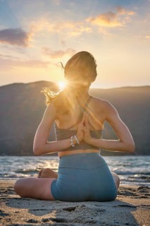A woman sits in Padmasana on the beach, hands in Pashchima Namaskarasana, soaking in the peaceful
