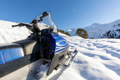 A blue snowmobile parked on a snow-covered slope against a backdrop of majestic winter mountains.