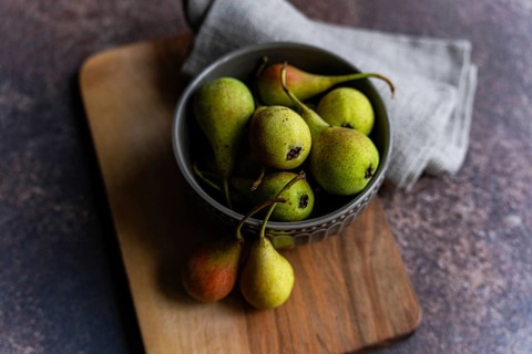 A rustic arrangement featuring a bowl filled with fresh wild pears. The pears exhibit a mix of