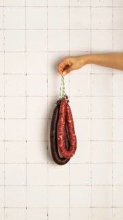 A hand holds black pudding and pork sausage against a white tiled wall, showcasing different
