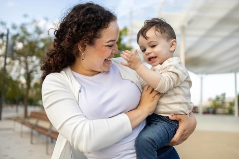 A joyful mother holding her baby in a park, enjoying a sunny day together. The scene captures a