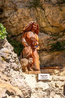 Wooden sculpture representing baba, a mythological creature, holding flowers and accompanied by a