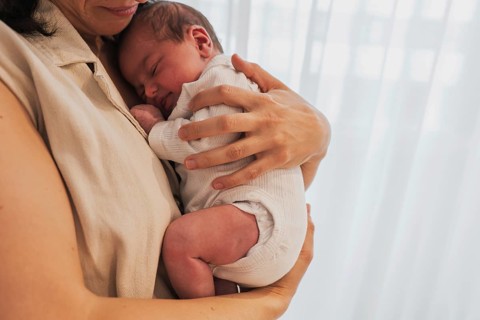 A young family enjoys a tender moment as the mother lovingly cradles a newborn against her chest.