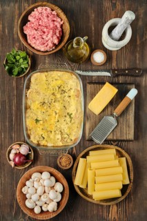 Fresh ground meat, vegetables, and spices arranged around a delicious baked pasta casserole in a