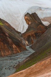 Steaming stream between colourful rhyolite mountains and snowfields, Hveradalir geothermal area,