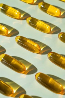 Multiple Omega 3 capsules arranged neatly on a light background, reflecting sunlight. The gel