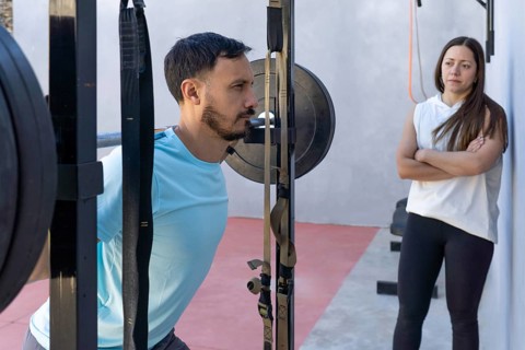Determined male athlete is lifting weights in a gym setting, performing squats with a barbell while