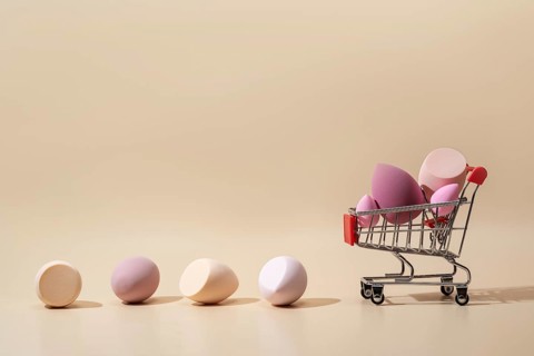 Soft cosmetic sponges in various pastel tones are displayed creatively in a miniature shopping cart