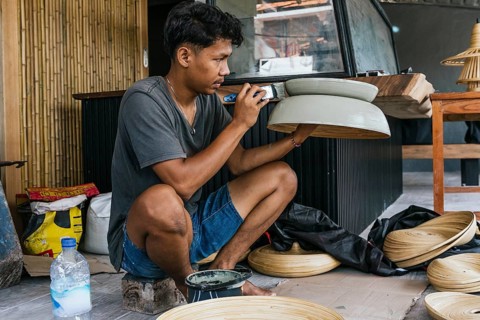 A Balinese artisan meticulously hand-paints a wooden sculpture in a vibrant workshop setting,